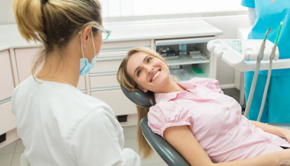 A Satisfied Woman After Dental Treatment Sits In Dental Chair And looks At The Dentist