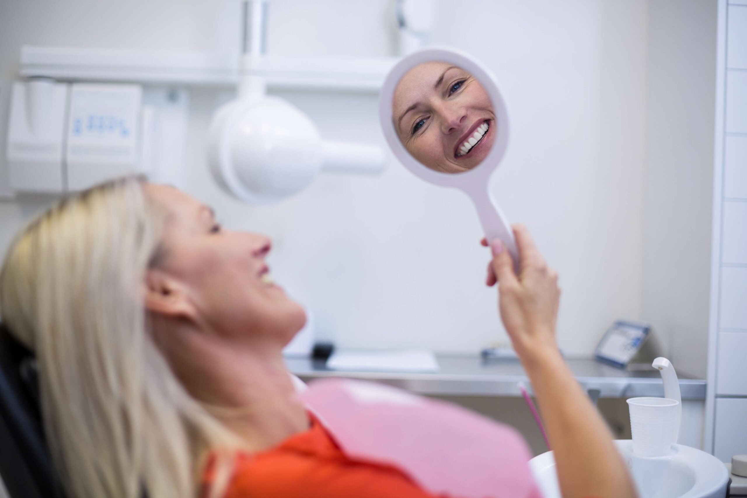 Patient smiling while checking teeth in a dental mirror after treatment.